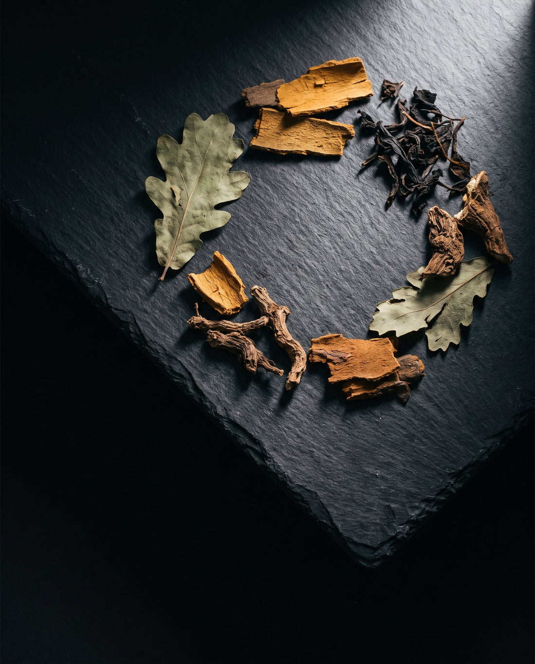 Dried leaves, bark and root pieces arranged in a ring on a dark slate tile