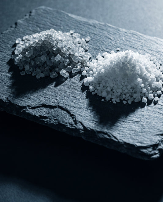 Two piles of coarse mineral crystals side by side on a dark slate slab