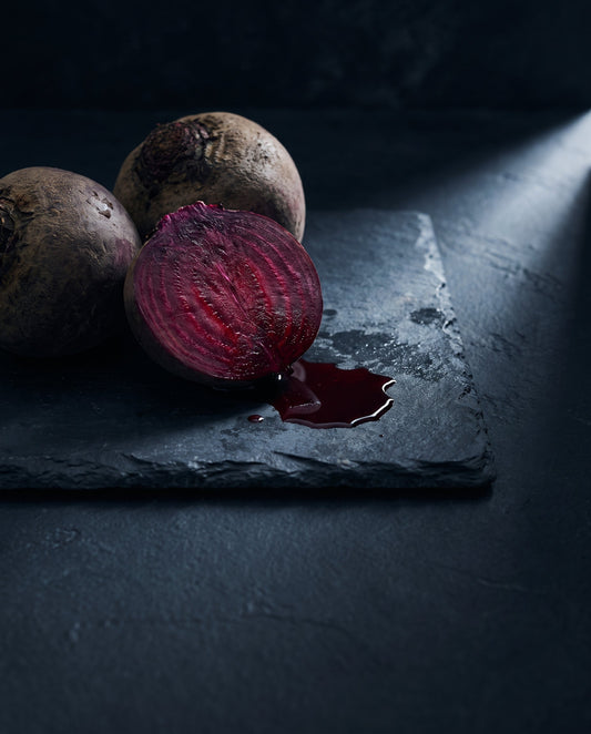 Whole and halved raw beetroot on dark slate, the cut face showing deep crimson rings